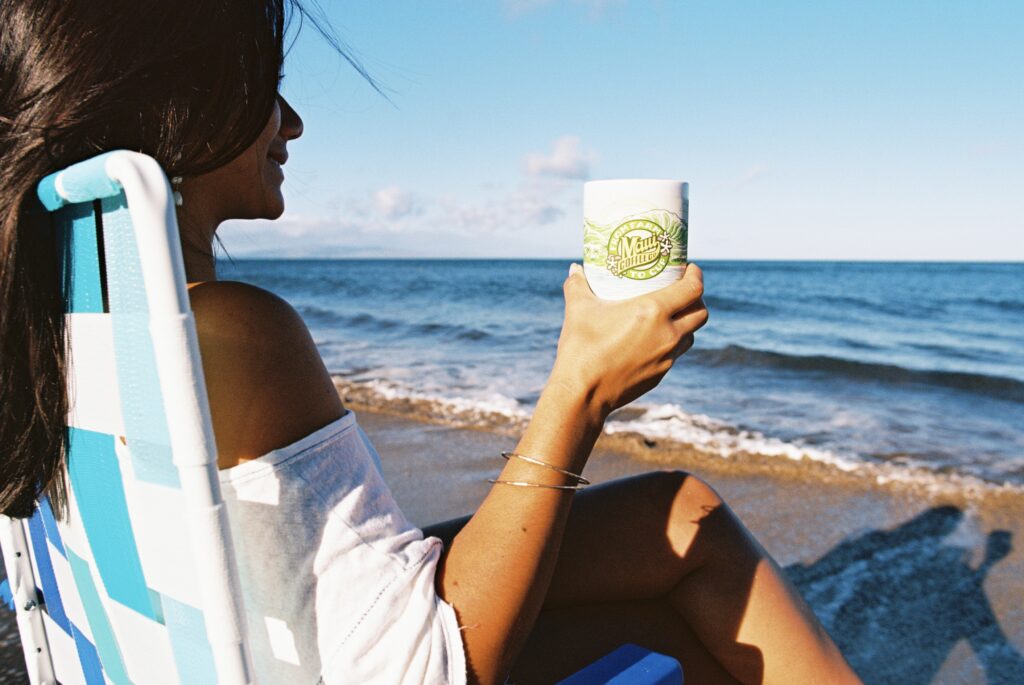 Coffee, Culture, & Conversation: Image of Girl Enjoying Maui Coffee in Maui Coffee Co. Mug By the Ocean