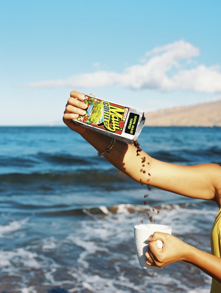 Fresh Insights from Paradise - 100% Maui coffee beans being poured into a cup by the ocean in Maui.
